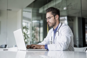 Male doctor using laptop at desk in clinic