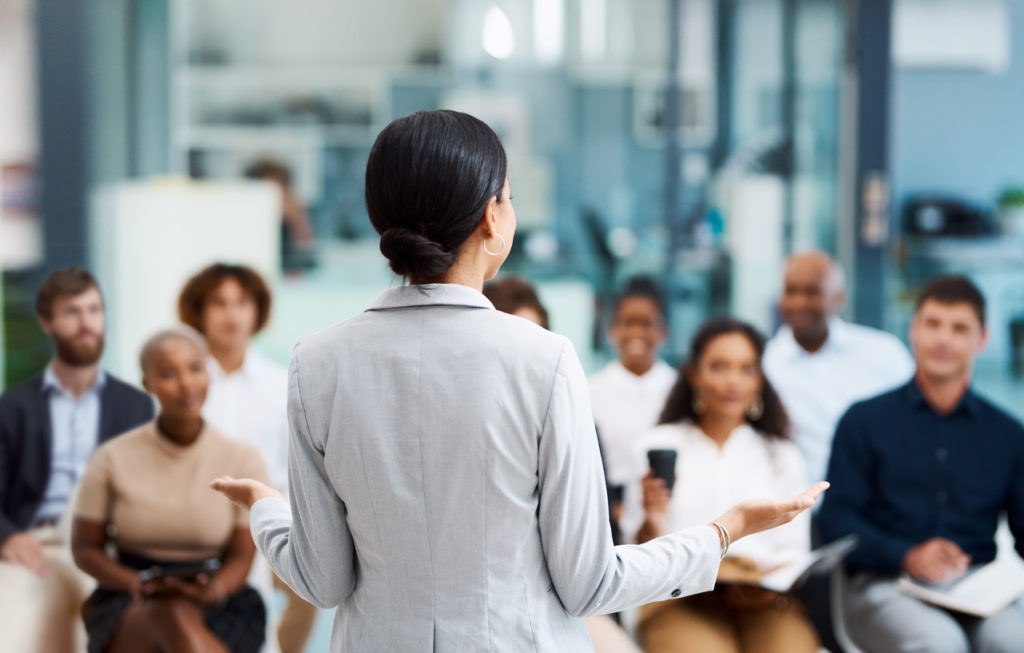 Lady standing in front of colleagues giving a presentation